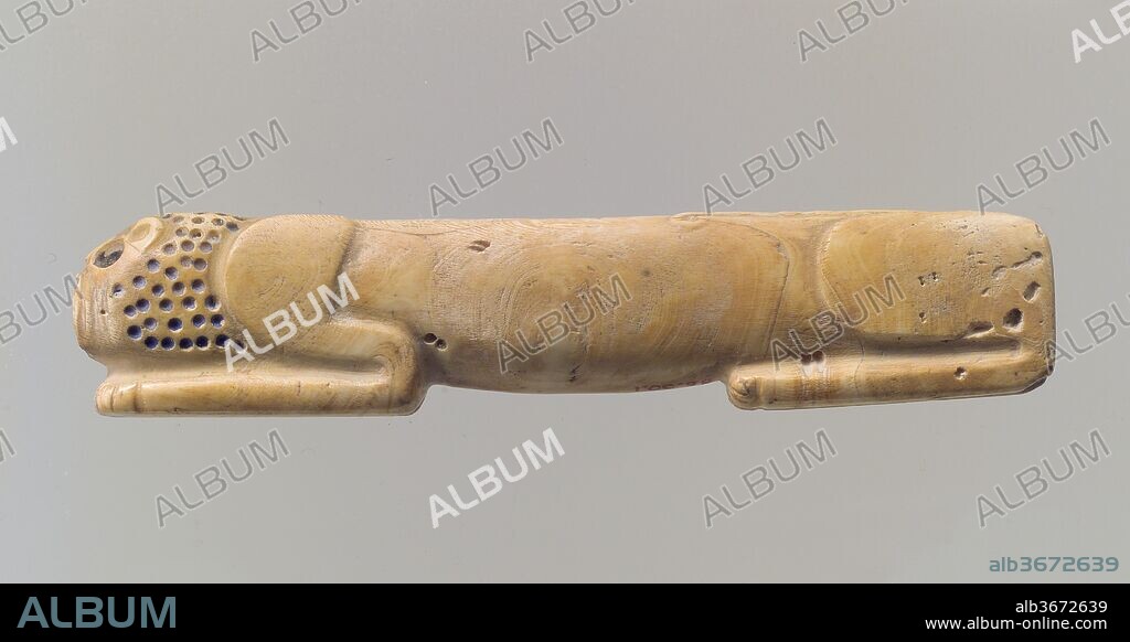 Amulet in the form of a couchant lion. Dimensions: 7/8 x 4 1/8 in. (2.2 x 10.6 cm). Date: ca. 2900-2700 B.C..
This small object carved from a piece of shell depicts a reclining lion with head resting on his front paws. The elements of the animal's body are very simply modeled: haunches, body, shoulders and front paws, and head can be identified. The back is straight and the belly hangs down slightly. Small drilled holes mark the mane, and larger holes indicate the eye and ear. Traces of pigment in these holes suggest that they were originally inlaid with a material in a contrasting color. Lions were one of the most frequently represented animals in the art of Mesopotamia from a very early period on, and were often shown in combat with an adversary, either human or supernatural. This object may have been used as an amulet, harnessing the enormous power of this fearsome animal.