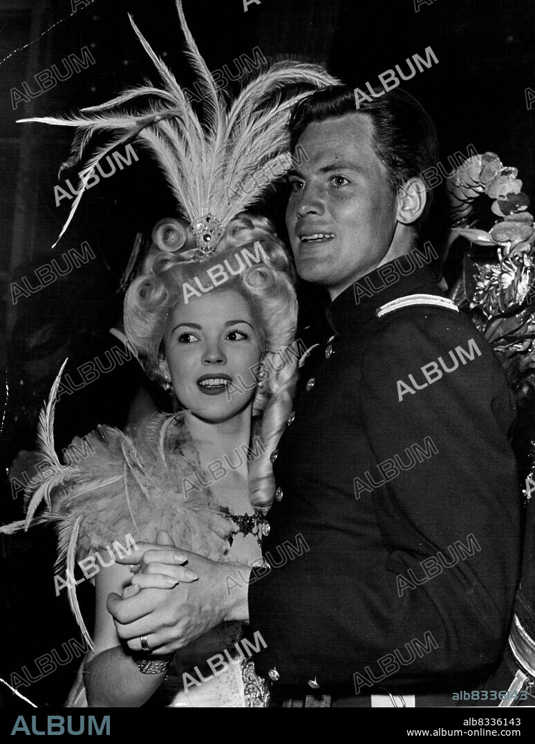 Shirley Temple dances in feathers while husband John Agar appears in the uniform he wears in RKO's forthcoming Fort Apache at a recent fancy dress party. December 19, 1948.