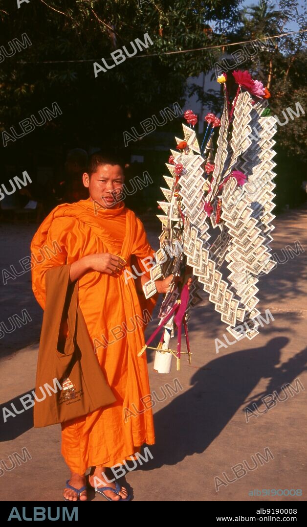 Laos: A Buddhist monk with a 'money tree' (used for making merit), Wat Sainyaphum, Savannakhet, southern Laos. At certain times in the Buddhist calendar, villagers and laypeople collect money to present to the monks in their local temple. This money is vividly arranged on a 'money tree'.