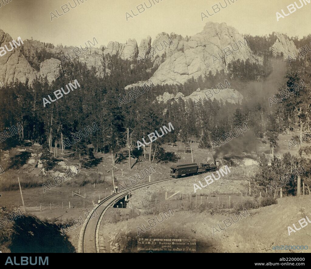 Bird's-eye view of a train on tracks, just beyond a marked curve. On Burlington and Missouri River Railway. Buckhorn Mountains in background.  Photograph by John C.H. Grabill in 1890.