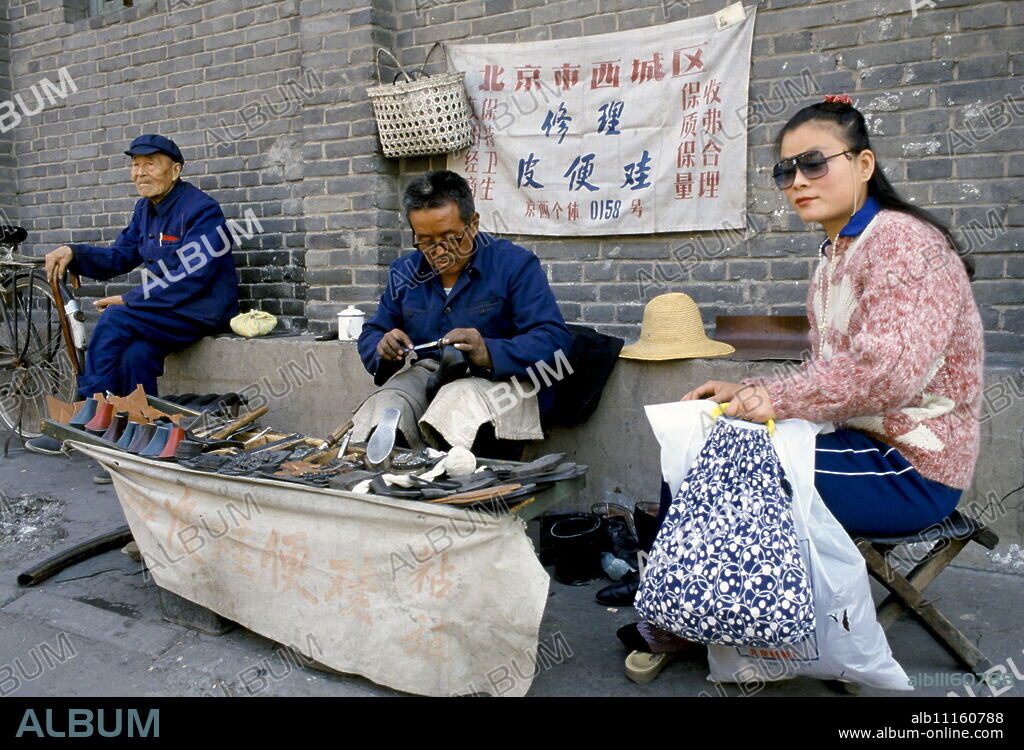 Chinese cobbler making and repairing shoes in backstreets of Peking, now Beijing, China in the 1980s.