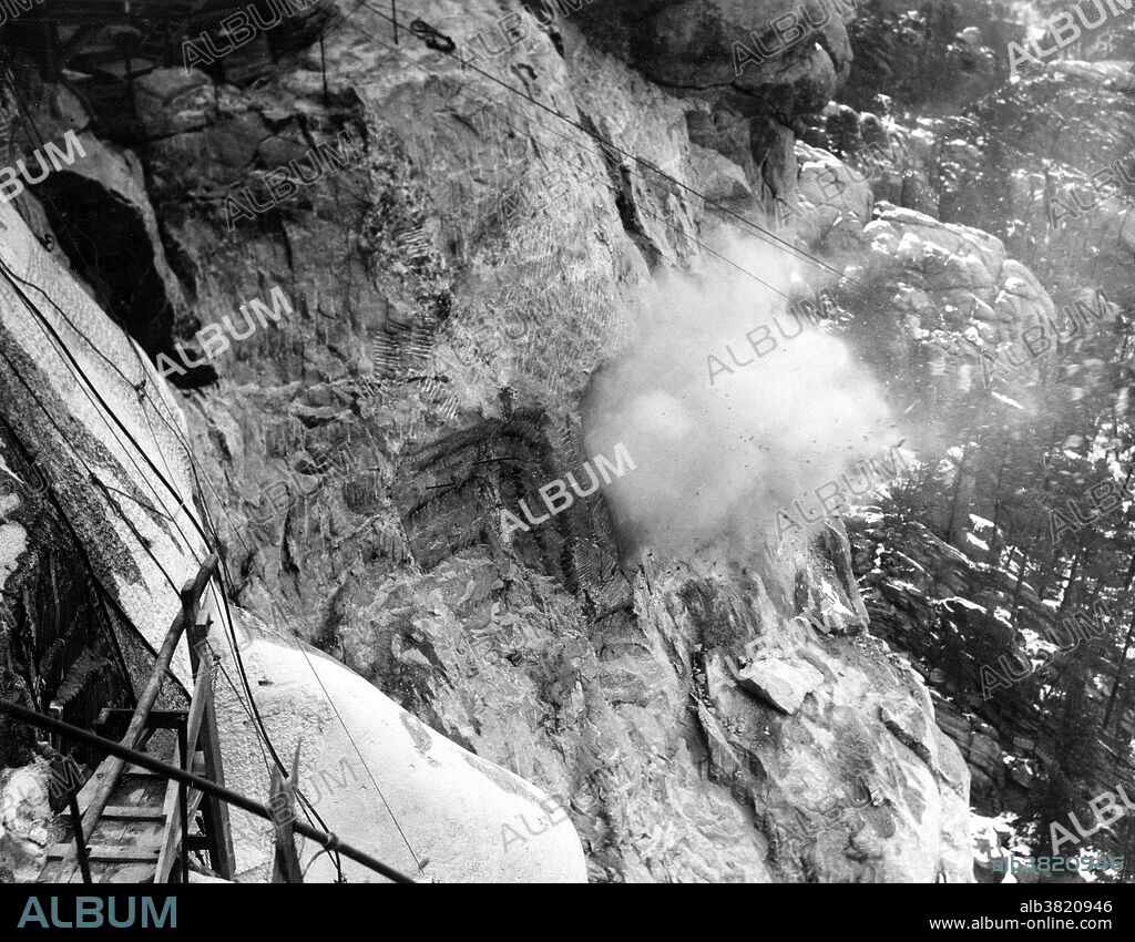Over 90% of Mount Rushmore was carved using dynamite. Dynamite blasts removed approximately 450,000 tons of rock from the mountain. Dynamite was used until only three to six inches of rock was left to remove to get to the final carving surface. At this point, the drillers and assistant carvers would drill holes into the granite very close together. This was called honeycombing. The closely drilled holes would weaken the granite so it could be removed often by hand. This historic photo is of early construction work on the Lincoln sculpture, showing dust from the dynamite blasts. Lincoln's head was the most challenging because of his beard, but his head was completed on the far right of the cliff. Mount Rushmore National Memorial is a sculpture carved into the granite face of Mount Rushmore near Keystone, South Dakota, featuring 60-foot sculptures of the heads of four U.S. presidents: George Washington, Thomas Jefferson, Theodore Roosevelt, and Abraham Lincoln. Construction on the memorial began in 1927, and the presidents' faces were completed between 1934 and 1939. Mount Rushmore has become an iconic symbol of the United States, and attracts over three million visitors annually. Photographed by Charles D'Emery, undated.