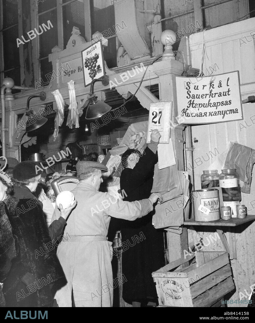 Stockholm 1954-03-27. Hötorget, gamla saluhallen. Fru Signe Hedin, en av de gamla, river av dagens datum medan de sista kunderna handlar.. Foto: DN / TT / Kod: 192. ** SvD OUT **.