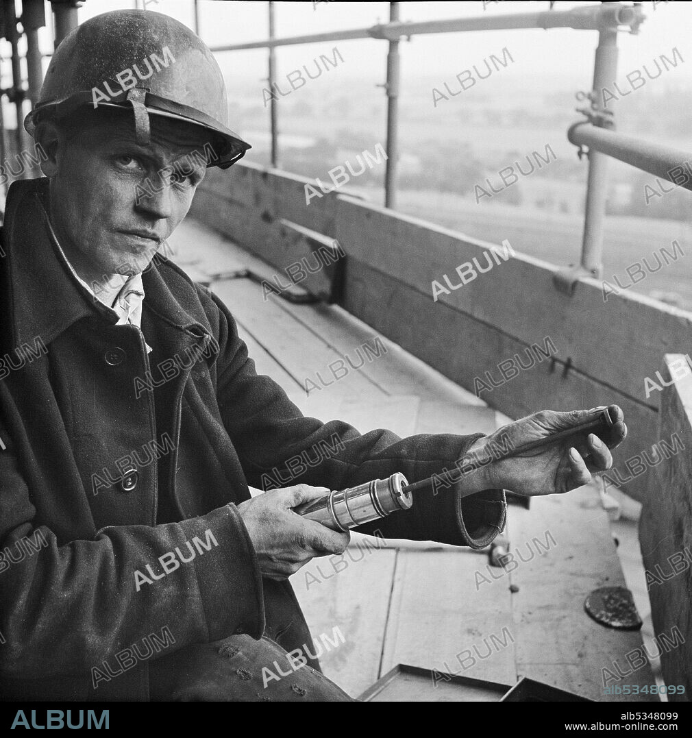 JOHN LAING PLC. A worker loading a riveting gun during the construction of two sugar silos at Poppleton Sugar Beet Factory. Two sugar silos were built by Laing for the British Sugar Corporation Limited at the Poppleton Sugar Beet Factory. They were designed to hold a total of 16,000 tons of sugar and were the largest to have been built in the country when this photograph was taken. The prestressed post-tensioned concrete silos were made with sliding formwork using hydraulic climbing jacks.