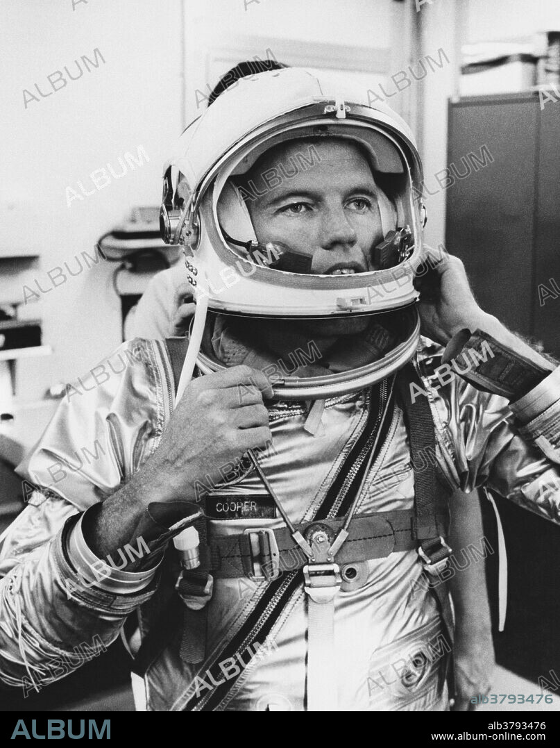 Astronaut L. Gordon Cooper puts on a helmet with a mechanical visor lock. The sealing system consists of a pivoted plexiglas visor, a pneumatic visor sea, and an on-off visor valve. Closing the visor actuates the valve and causes automatic inflation of the seal.
