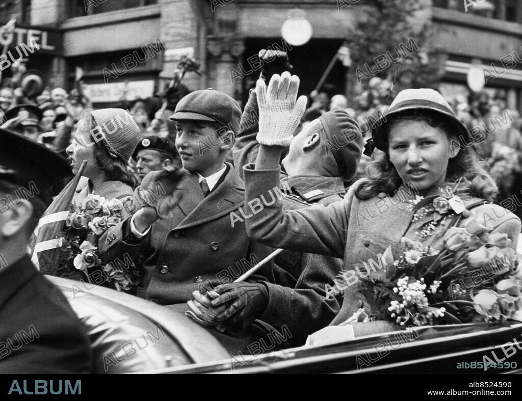 ARKIV 1945. Norska prinsessan Astrid, av Norge t.h. vinkar med blommor i handen i bilen tillsammans med sina syskon prinsessan Ragnhild, t.v. och kronprins Olav, vid Kung Haakons återkomst till Norge efter landsflykten under andra världskriget.. Foto: Reportagebild / SCANPIX / Kod: 37770.