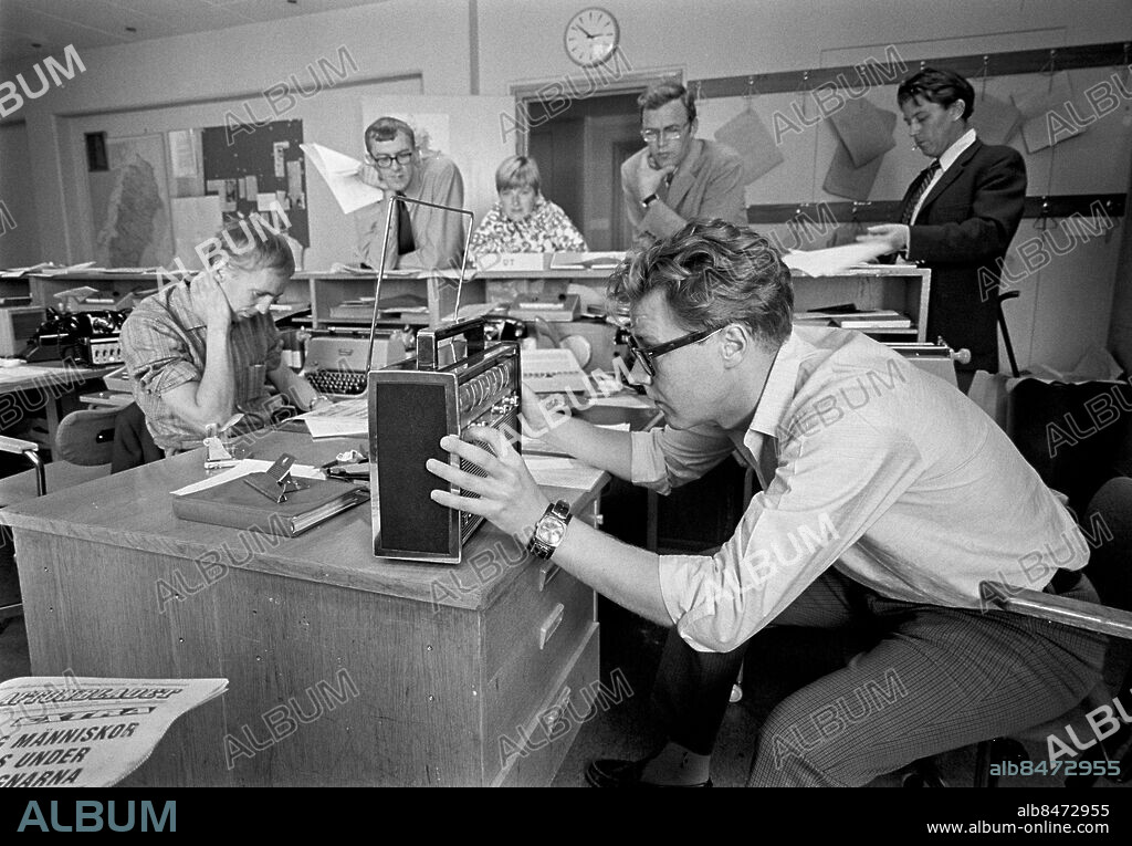STOCKHOLM 1968-08-21.. Ett extraeko ska snart sändas med anledning av ockupationen av Tjeckoslovakien. En liten del av ekoredaktionen är samlad. Sven Valtersson läser en kvällstidning. Mitt emot honom försöker Olle Tolgraven få in en tjeckisk radiostation. Berndt Ahlqvist, Pia Brandelius, Arvid Lagercrantz och Sven Sjöberg avvaktar i bakgrunden.. Foto: Bo-Aje Mellin / RiR / SVT / Kod: 5600. Bild och reportage publ. i RiR 36/68 sid. 46.. RiR 19137 sv/v neg.