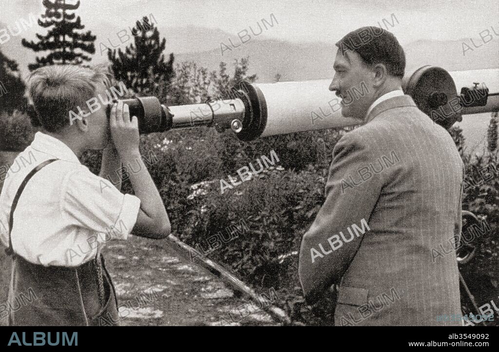 Adolf Hitler at his residence in Obersalzberg, Bavaria, Germany in 1936, watching a boy observing the Unterberg Mountain through a telescope. Hitler believed that the mystical powers of the mountain would help him defeat his enemies. Adolf Hitler, 1889 – 1945. German politician, leader of the Nazi Party, Chancellor of Germany and Führer ("leader") of Nazi Germany.