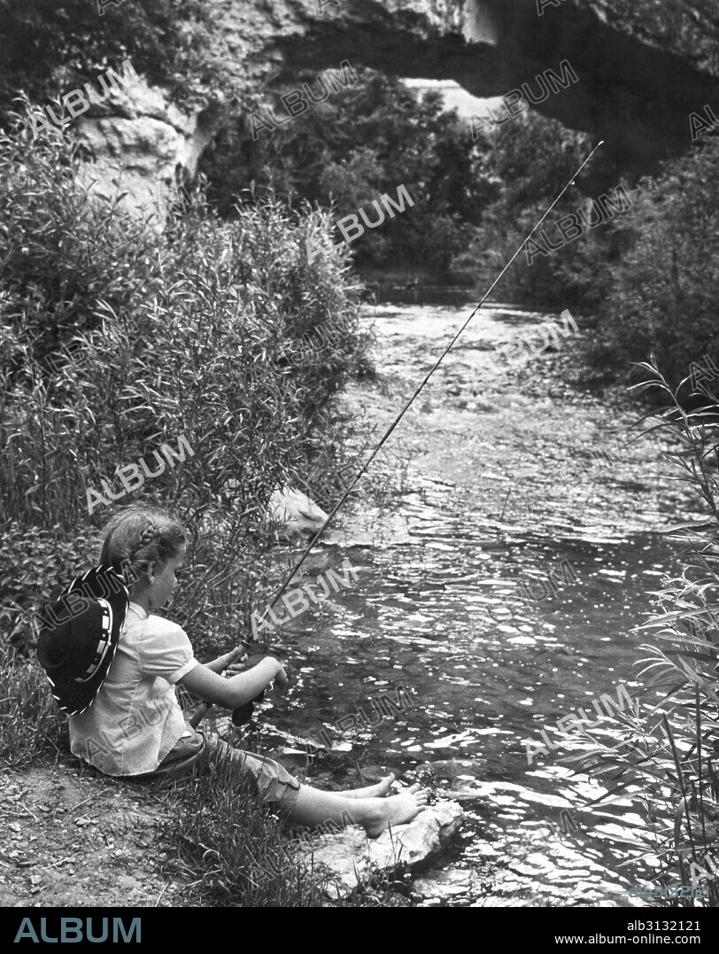 United States:  c. 1954 A young barefoot girl fishing in a small stream.