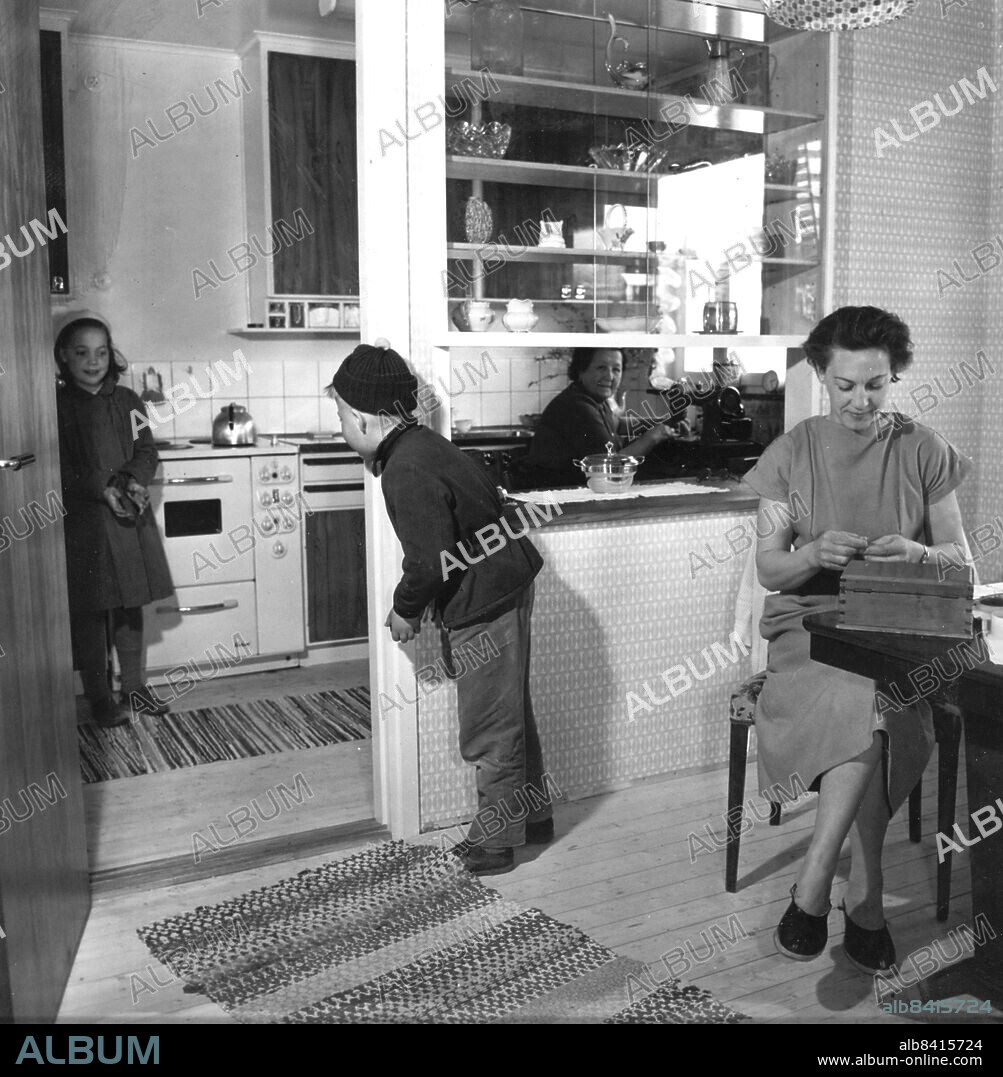 Stockholm 1957-04-26. Hyreslägenhet i Hässelby gård. Fru Dagny Olsson sitter vid matbordet i allrummet, där barnen Renee och Kent-Åke har sin lekpats. Bakom bardisken sitter vid arbetsplatsen i köket fru Hilma Karlsson.. Foto: Boris Engström / DN / TT / Kod: 192. ** SvD OUT **.