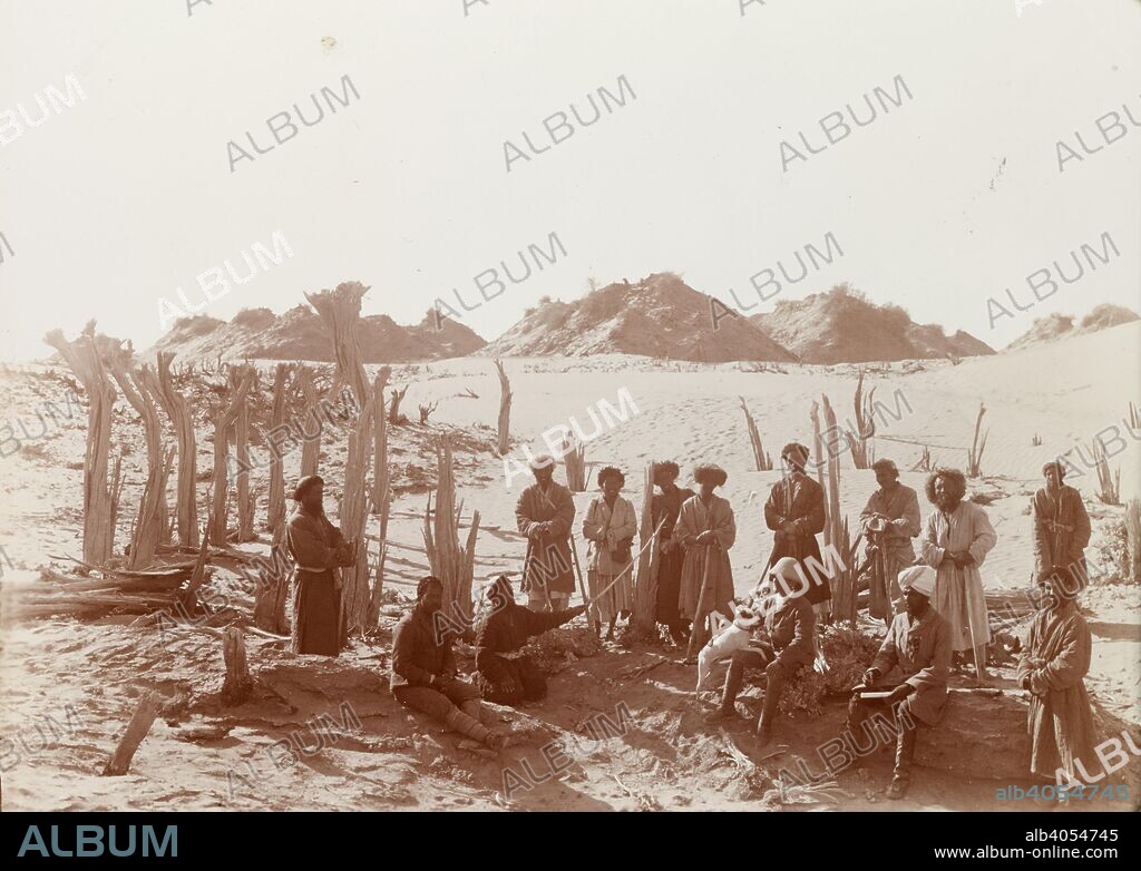 SIR MARC AUREL STEIN. Group portrait at the Niya site. 1906. Trunks of dead trees enclosing ancient tank, Niya site. The group shows, sitting on the left Rai Ram Singh and Ibrahim Beg, on right Naik Ram Singh and Ibrahim 'the miller'. Stein sits in the middle with his dog, Dash.  Originally published/produced in 1906. . Source: OIOC Photo 392/27(97),.