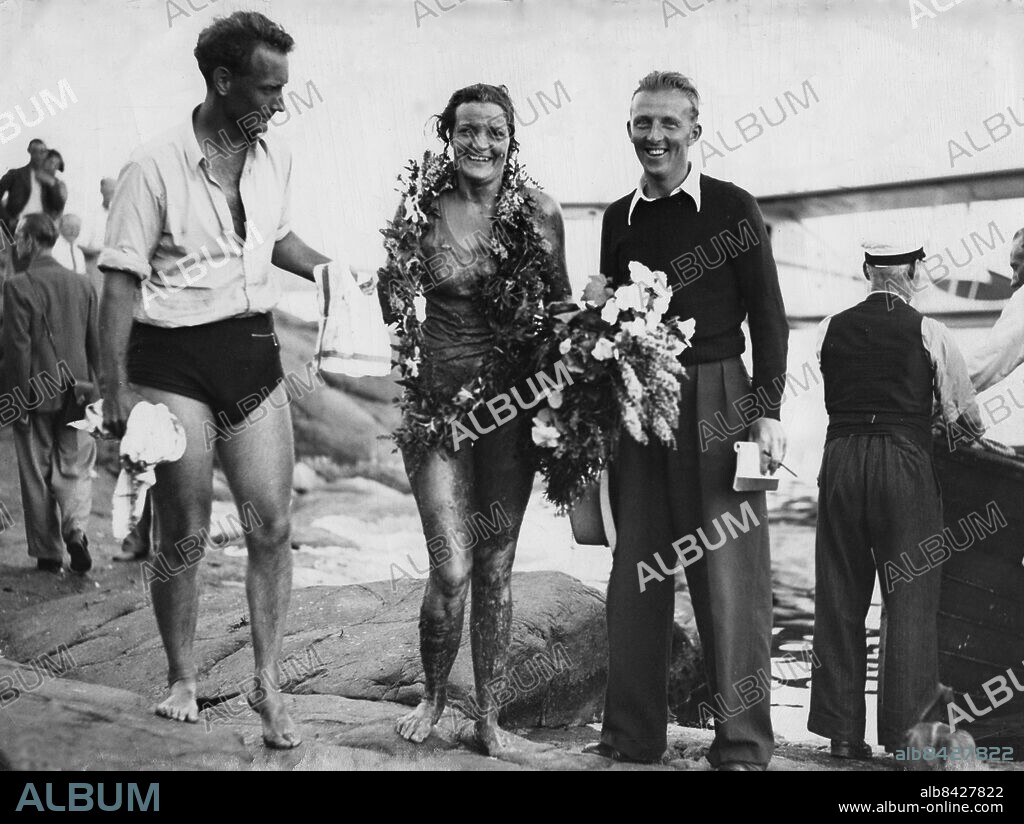 ARKIV 1939 . Sally Bauer, 18-årig simmerska, hjälps i land sedan hon slagit rekord i långdistanssimning över Ålands hav - en sträcka hon klarade på tretton timmar och sex minuter. På bilden gratuleras hon av bl a tidningsmannen och författaren Staffan Tjerneld.. Foto: NTB kod 194. ***SVD OUT***.
