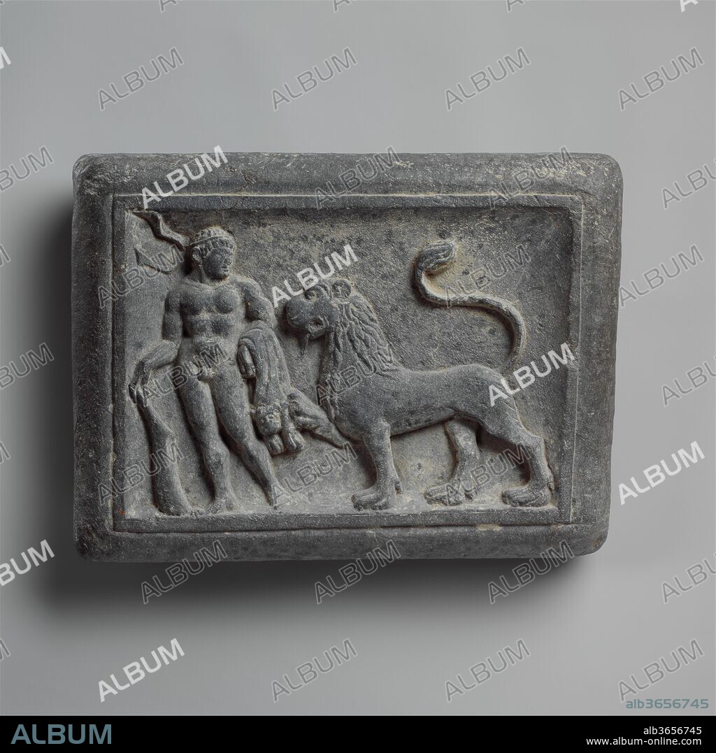 Wrestler's Weight with Hercules and the Nemean Lion; Wrestling Scene (reverse). Culture: Pakistan (ancient region of Gandhara). Dimensions: 10 1/4 x 13 3/4 in. (26 x 34.9 cm). Date: ca. 1st century.
As the first of his twelve labors, the Greek mythic hero Herakles was ordered to slay the monstrous Nemean lion. Since the beast's skin was impervious to spears and arrows, Herakles strangled him. He then skinned the lion, taking the pelt as a cloak and the head as a helmet. The lion skin slung over his left arm suggest that the figure on this weight is Herakles, although there is no obvious explanation for the charmingly tame lion that accompanies him. Two half-moon shaped indentations for gripping at the back (not visible) indicate that this object is an athlete's weight.