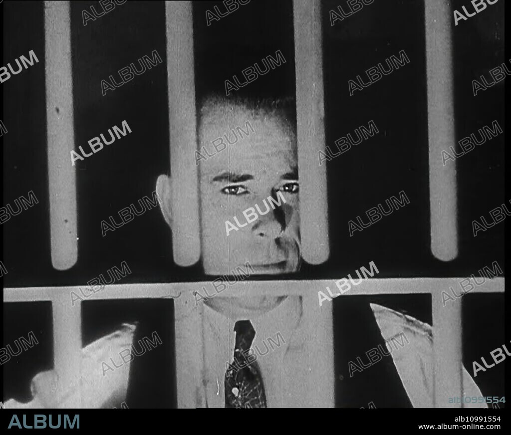 American Gangster John Dillinger Behind Bars, 1930s. Dillinger (1903-1934) commanded the Dillinger Gang, which was accused of robbing twenty-four banks and four police stations. He was imprisoned several times and escaped twice. From "Time To Remember -  The Tough Guys", 1930s  (Reel 2); documentary film, mainly about life in depression- and gangster-hit America.