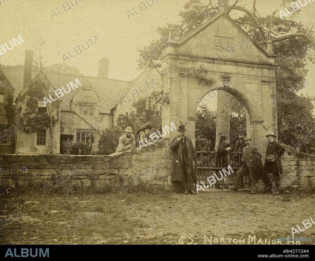Bredon's Norton Manor, Bredon, Wychavon, Worcestershire, 1880s. A group of men standing in front of the stone gateway of the manor house, with a further group standing at the doorway in the background. The gateway shown in the photograph is referred to in Victorian County History: Worcestershire vol 3 (1913), where it mentions that the gateway was blown down about 25 years ago and was carefully re-erected. As this photograph shows no datestone on the gateway but later photos do, it appears likely that this was taken before it was re-erected and a new datestone possibly carved at the same time.