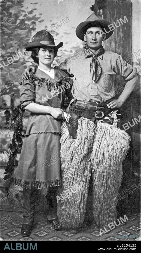 United States:   c. 1900. A couple pose for a studio portrait in Western cowboy gear.
