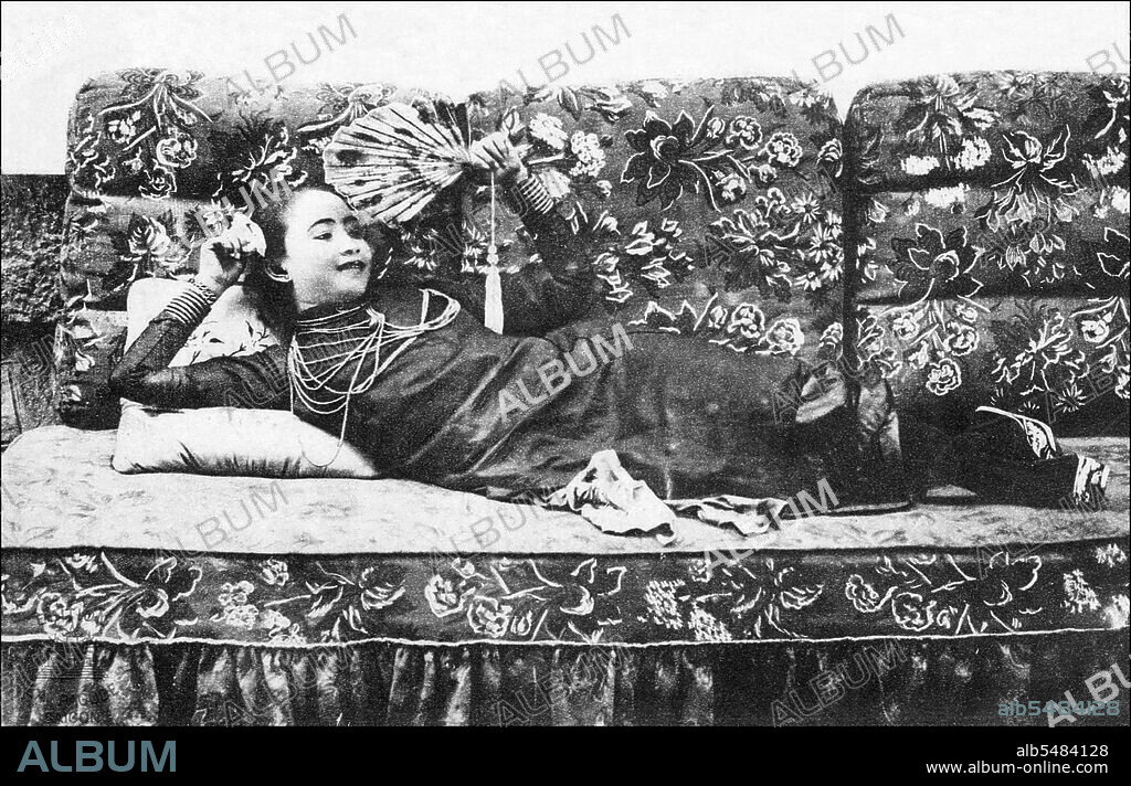 Studio photograph of a Vietnamese prostitute reclining on a bed with a fan, Saigon, c.1910.