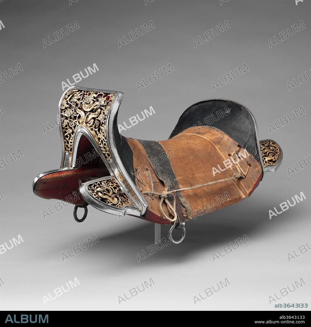 Saddle (gser sga). Culture: Eastern Tibetan or Chinese for the Tibetan market. Dimensions: H. 10 3/4 in. (27.3 cm); L. 22 1/2 in. (57.2 cm); W. 11 3/4 in. (29.8 cm). Date: 17th-18th century.
This saddle represents a particular form found in Tibet, one that is Chinese or strongly influenced by Chinese types. It belongs to a small group of closely related saddles that may stem from a single workshop or reflect a specific type developed in one region. Notable features are the lively dragons, chiseled free from the scrollwork ground, and the unusual decorative technique involving silver damascening of the entire surfaces of the saddle plates, with select design elements highlighted by mercury gilding over the silver. Also very distinctive is the use of three layers of decoration: the outer layer of pierced scrollwork with long tendrils deeply undercut to give an appearance of depth, a second layer forming a subsidiary ground underlying each saddle plate and consisting of an iron grill damascened in silver to create a stylized cloud pattern, and a layer of colored cloth directly on top of the wood of the saddle-tree.