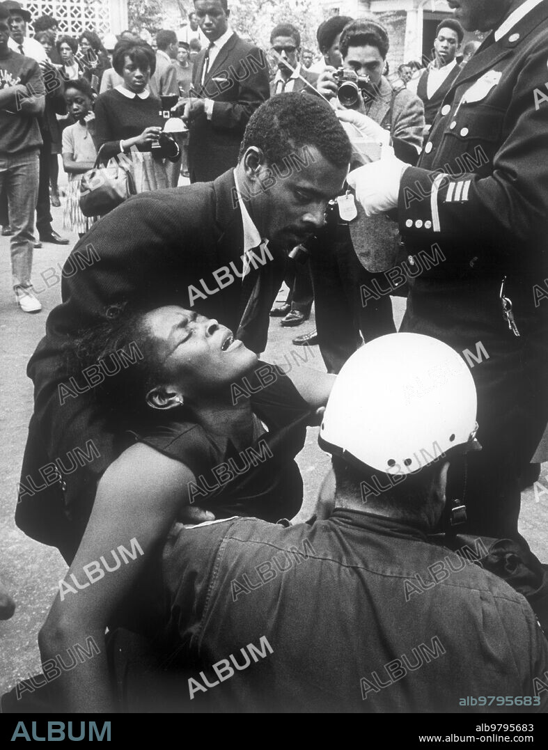 Fainted woman helped by a friend and a police during the funeral march for martin luther king, at lanta, 1968.