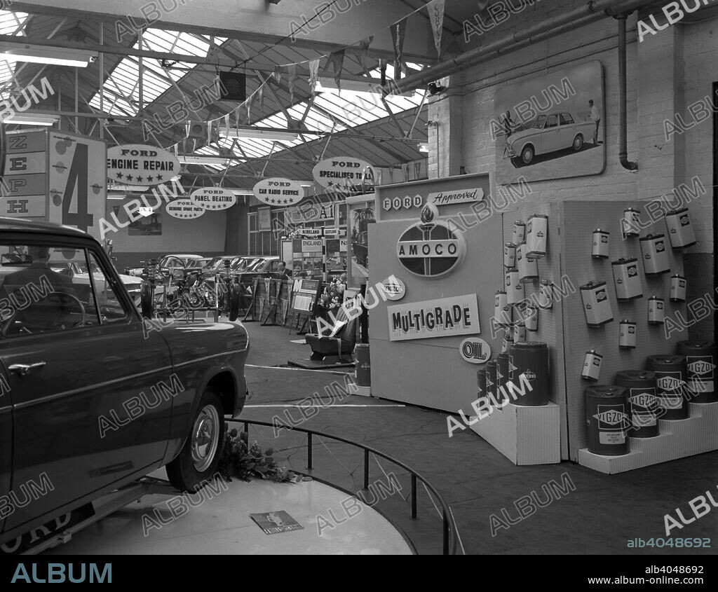 Exhibition at a Ford dealers in Rotherham, South Yorkshire, 1964. A photograph showing Amoco's range of Vigzol motor oils on a display stand on the right hand side of the photograph. A range of other Ford cars can be seen including an Anglia in the foreground, and what appears to be a body off chassis behind it. In the background sits an Anglia from the 1950s and a couple of Consuls. Signs hang from the ceiling in the background advertising the various motor maintenance services on offer.