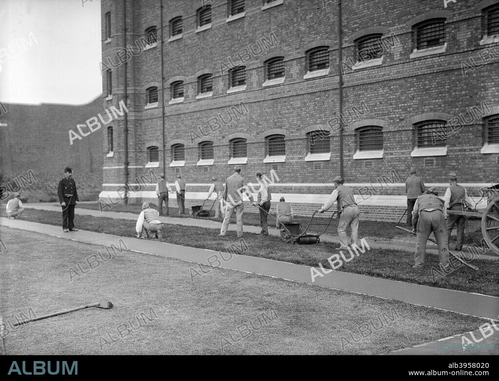 Prisoners cutting grass at Wormwood Scrubs prison, London, c1900-1950. Various parts of the 'Scrubs' were built using prison labour between 1874 and 1891. It was the first prison to use the Telegraph Pole layout. Here prisoners are working on the prison gardens. Note that the uniforms of the inmates still bear their characteristic arrows.
