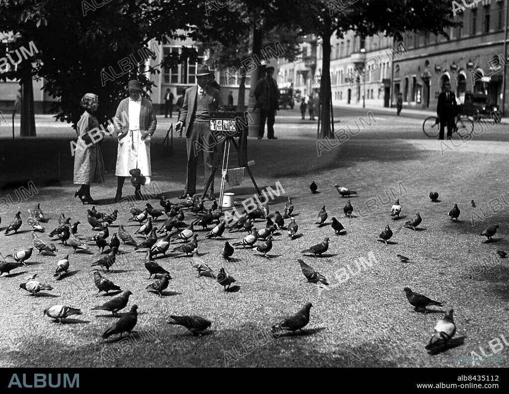 Arkiv 1934 . Kanonfotograf var en fotograf som yrkesmässigt fotograferade ögonblicksbilder på folk (ofta turister) på offentliga platser i staden. Kanonfotografen började bli ett vanligt inslag i stadsbilden på 1930-talet.. Street photographer in Stockholm.. Foto: TT / Kod 1900.
