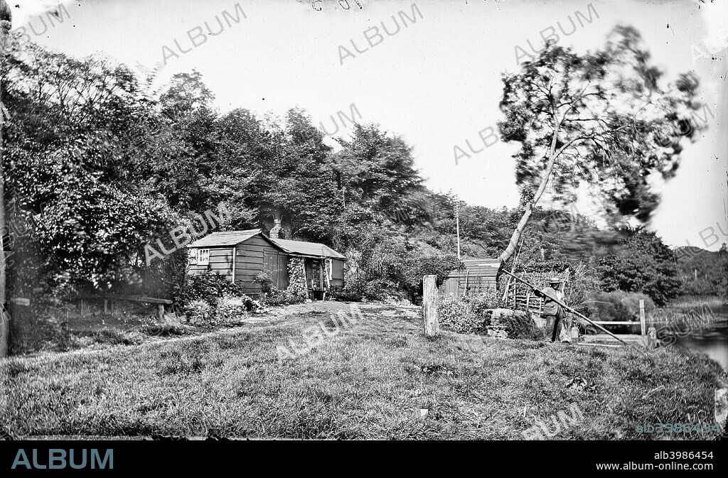 Roebuck Ferry House, Purley On Thames, Berkshire, c1860-c1922. The ferryman on his boat on the River Thames, with his small wooden house on the bank above.