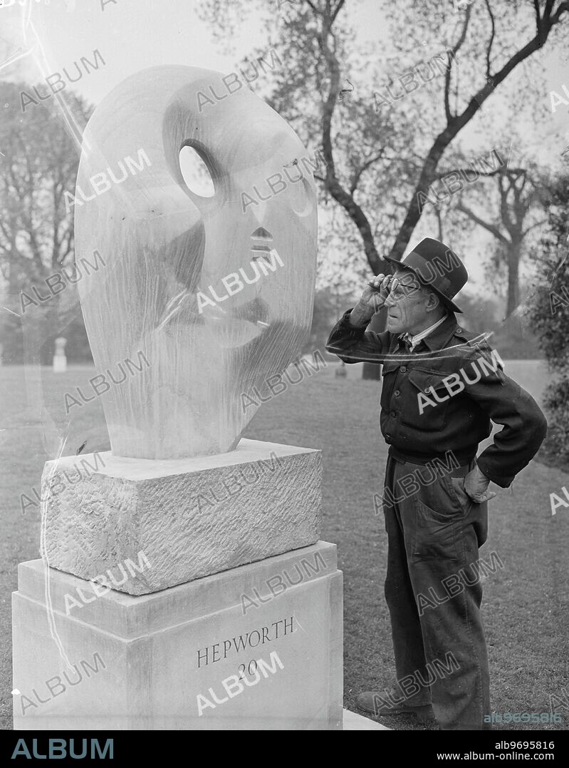 A puzzled Battersea (South London) park-keeper, Mr C Barnard, takes a second look - this time without spectacles - at " Biolith ", a Blue Ancaster stone sculpture by Barbara Hepworth, on show at the Second International Open Air Exhibition of Sculpture in Battersea Park, London. The Exhibition - the first was held in 1948 - has been organised by the London County Council in Association with the Arts Council of Great Britain. Barbara Hepworth, who has done some work for the Festival of Britatin's South Bank Exhibition, was born in Wakefield, Yorkshire, in 1903, and she now lives in Cornwall. 7 May 1951.