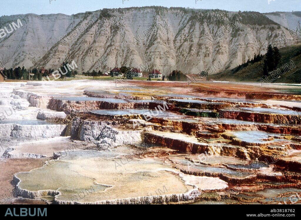 Hymen Terrace, Mammoth Hot Springs, with Fort Yellowstone in the background. Detroit Publishing Company, 1902. View of Hymen Terrace at Mammoth Hot Springs. Shows thermal pools and terraces, the Liberty Cap, an extinct hot spring cone, and two-story buildings with red roofs, probably Fort Yellowstone. Mammoth Hot Springs is a large complex of hot springs on a hill of travertine in Yellowstone NP adjacent to Fort Yellowstone and the Mammoth Hot Springs Historic District. It was created over thousands of years as hot water from the spring cooled and deposited calcium carbonate (over two tons flow into Mammoth each day in a solution). Although these springs lie outside the caldera boundary, their energy has been attributed to the same magmatic system that fuels other Yellowstone geothermal areas. Yellowstone National Park is a national park located primarily in the state of Wyoming, although it also extends into Montana and Idaho.