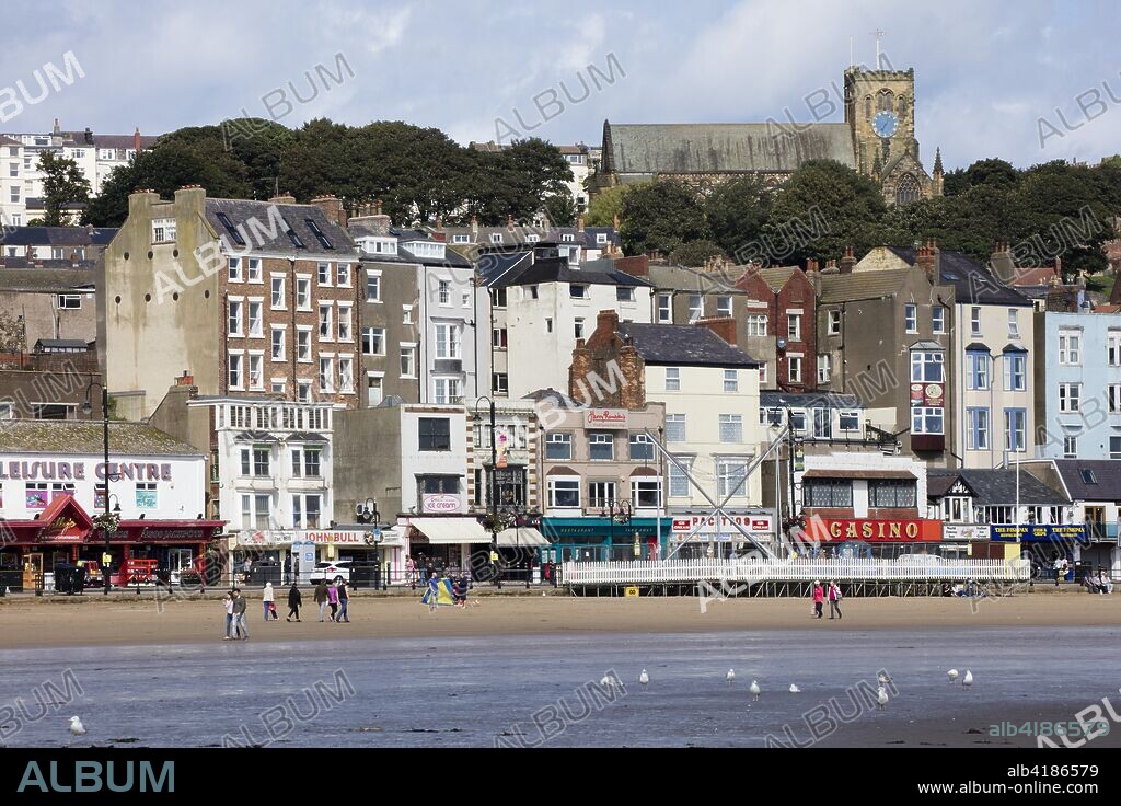 Foreshore Road, Scarborough, North Yorkshire, 2017. General view looking north-west from the beach towards shops, cafes and amusement arcades at the north end of the street, with St Mary's Church in the background.