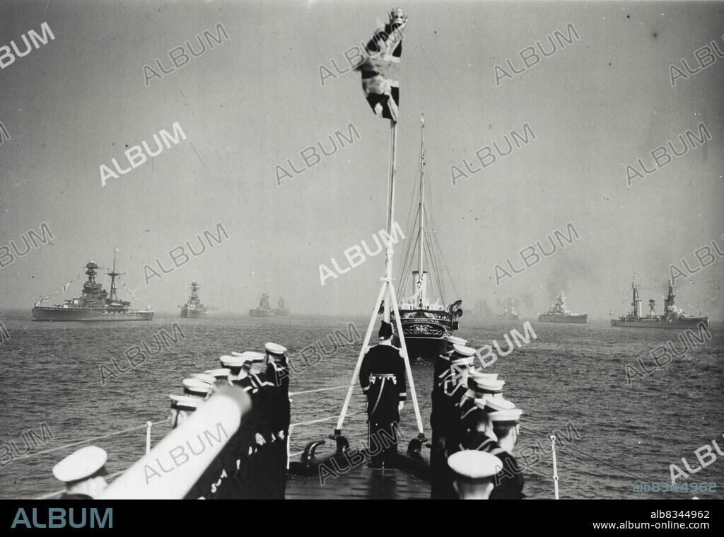 The King Reviews His Fleet - H.M. King George VI to-day reviewed the ships of the British Navy at Spithead, Portsmouth.The Royal yacht, Victoria & Albert, passing down the lines of battleships. In background left to right are - H.M.S. Royal Oak, H.M.S. Rodney, H.M.S. Helson, U.S.N. New York, Dunkerque (France), Moreno (Argentine). In foreground is bow of the Admiralty yacht Enchantress. June 14, 1937. (Photo by Topical Press).