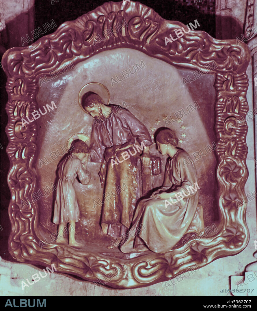 LLIMONA, JOSEP (1863-1934); GAUDI, ANTONI (1852-1926); OLIVA, ANTONI. Sagrada Familia (Crypt): Altarpiece of the central altar of the sculptor Josep Llimona, with the frame made by Gaudí and decorated by Antoni Oliva. This altarpiece represents the Holy Family with the adolescent Jesus kissing St. Joseph's hand in front of a carpenter's table, while the Virgin watches the scene. At the top of the golden frame Gaudí put the inscription "amen" that also appears on the sides along with the anagram "JMJ" in reference to Jesus, Mary and Joseph. This relief is identical to the oak wood that was in the oratory of Casa Batlló, also by Josep Llimona, and that is now in the chapel of the Sacrament of the same temple. 1906.
