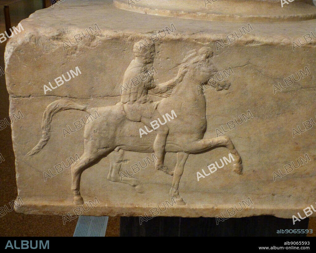 Base of a dedication in Marble. Found in the Athenian Agora. Base of a dedication for victories in the mock cavalry battle contest. Three sides of it have reliefs depicting a horseman riding toward a tripod. The inscription on the fourth side supplies the names of the victorious dedicators and also that of the sculptor Bryavis who carved the monument. It will have supported a bronze tripod dedicated by the victors. Middle of the 4th century BC.
