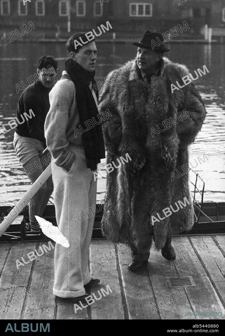 Boat Race Trainer's "New Look" -- Mr. Haig-Thomas chatting to the Oxford president, P.M. Brodie, at Henley. Behind them is the Australian members of the crew, L.S. Williams. Mr. Peter Haig-Thomas, who has not taken over the Oxford crew at Henley after a period of training the Cambridge crew, turned out yesterday adequately dressed to combat the cold weather - he was wearing a long, heavy, fur coat. Oxford boat crew trainer Peter Haig-Thomas in his shaggy New Look" outfit he uses for training in the cold weather. February 19, 1948. (Photo by Fox Photos).
