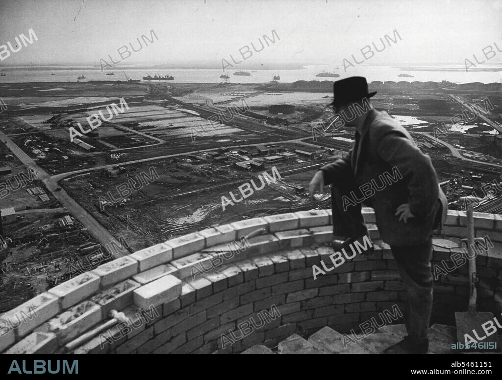 Abadan Moves To The Thames Oil Town For The Isle of Grain -- From one of the chimneys now being built on the Isle of Grain for the new oil refinery, and Anglo-Iranian oil company official has a grandstand view of the present transformation of the marshes. The river Medway is seen in background.At the mouth of the rive Thames Lies the Isle of Grain, a Marshy Island on which the Anglo-Iranian oil company is building a new Abadan. On salt-flats which for centuries have known little by the cry of seagulls, a huge refinery is springing up which by 1953 will be processing 4,000,000 tons of crude oil a year. March 6, 1952. (Photo by Paul Popper).