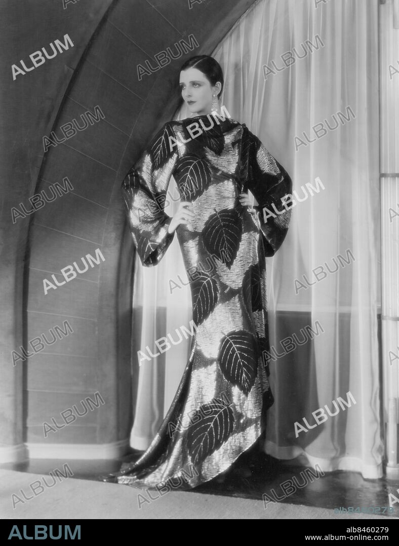 Orig. bildtext... FOR WEAR WITH THE AFTERNOON TEA. Hollywood, Calif. Mona Maris. Metro-Goldwyn-Mayer star, wears this exotic tea gown of black and gold brocade, fashioned in sophisticated lines and ending in a train. Anm. M Maris, 1903-1991, skådespelare från Argentina Klänningar Aftonklänningar Långklänningar Brokad Guld Örhängen Posering Mönster Löv Lyx CD361 persons: MONA MARIS sites: ARGENTINA*;HOLLYWOOD;USA.
