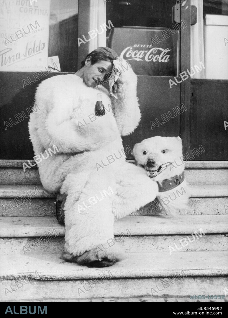 Orig. bildtext... HAN SOM INTE FRÖS I CORTINA! Den ende som inte frös under denna köldens olympiad var en till isbjörn kostymerad italiensk clown. Han roade publiken på gatorna och i pauser mellan de olika idrottsevenemangen och gjorde allt för att få temperaturen att stiga hos den huttrande publiken. När andra hackade tänder i den trötta alpsolen, tappade han ibland huvudet för att släcka törsten. Anm. OS i Cortina 1956 Vinter-OS Coca-Cola Flaskor Automater Utklädd Utklädningsdräkter Ansiktsuttryck Torkar svetten i pannan Svettas CD326 sites: ITALIEN;CORTINA.