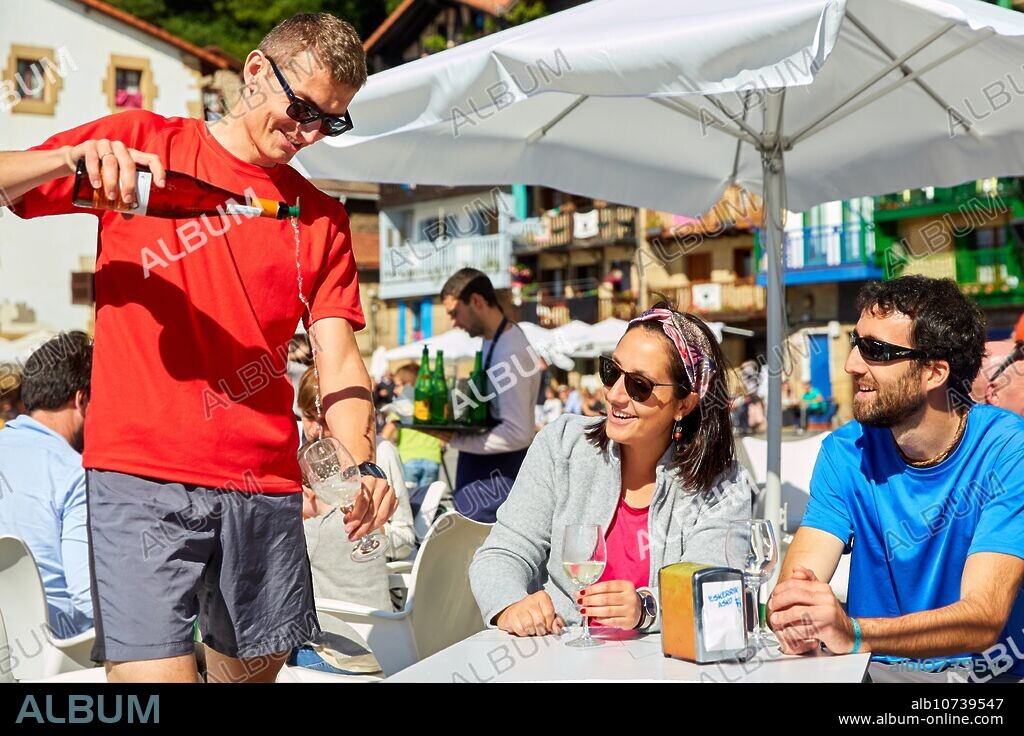 Guide with tourists having a wine, Txakoli, Plaza Santiago, Pasai Donibane, Pasajes de San Juan, Gipuzkoa, Basque Country, Spain, Europe.