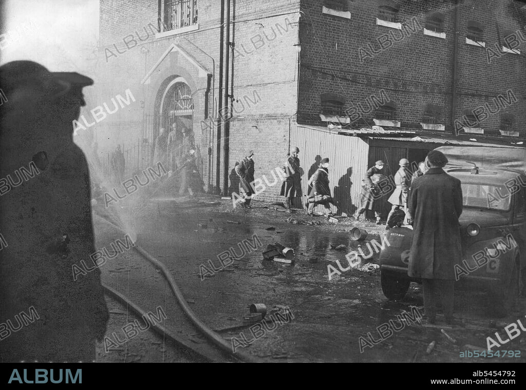 Soldiers Riot At Aldershot Detention Barracks -- "The Surrender" Men leaving the "The Glass House" under strong guard, while Fireman are fighting a fire started by the rioters. Picture taken Sunday. Military prisoners in Aldershot detention barracks last night started to riot. Some climbed to the roof of the main building and Firemen had to deluge them with water. They caused damage to the building in which they were held, smashing glass windows in the roof and skylight. February 24, 1946. (Photo by Reuterphoto).