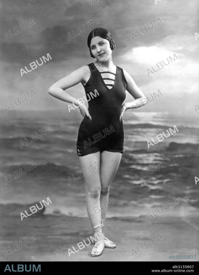 Paris, France:  c. 1920. A pretty woman in a bathing suit poses in front of a studio ocean scene.