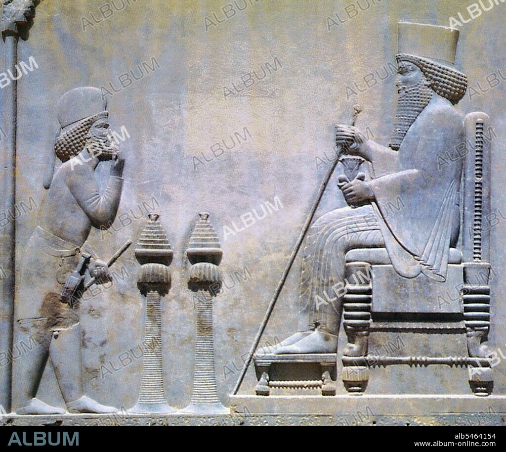 Darius I (550 – 486 BCE), also known as Darius the Great, was the fourth king of kings of the Achaemenid Empire. Darius held the empire at its peak, then including Egypt, Balochistan, Kurdistan and parts of Greece. The decay and eventual downfall of the empire commenced with his death and the ascension of his son, Xerxes I. This is a relief of the Persian King Darius I seated on a cushioned throne and holding a staff and flower, two traditional symbols of royal power in Persia. The subject approaching Darius to offer tribute stands behind two incense burners, which were intended to keep visitors a respectful distance from the king.
