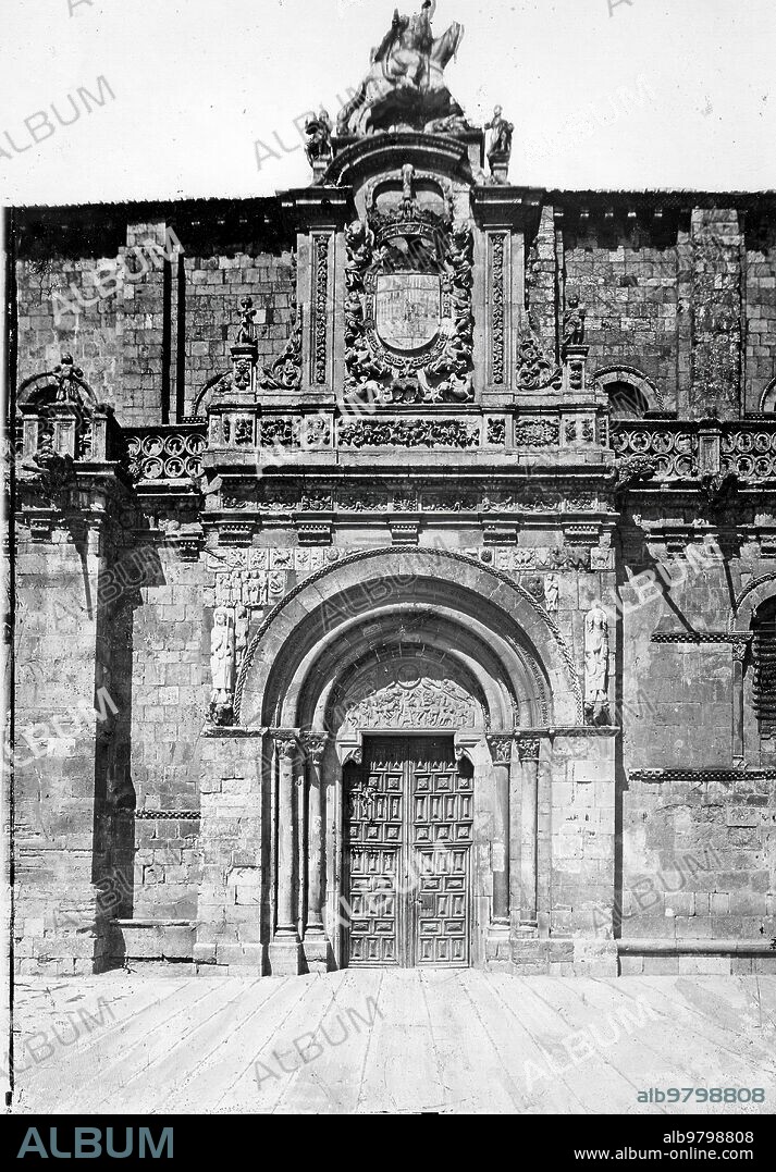 León, 1883 (CA.). Puerta principal de la Colegiata de San Isidoro. Esta se denomina Puerta del Cordero, ya que éste es el tema principal que aparece en el tímpano: el Cordero Místico sostenido por los Ángeles, el Sacrificio de Isaac, Sara a la puerta de la tienda e Ismael el arquero cabalgando por el desierto. A la izquierda figura San Isidoro, a la derecha san Pelayo y completan el programa iconográfico, el rey Daid, cinco músicos y los signos del zodiaco. En el reerso de la foto aparece el sello fotográfico de Ruiz Vernacci (Madrid) y en el pie de la foto, la fecha de la publicación (03/01/1932). También aparece firmada por Winocio Testera, por lo que se deduce que es una reproducción fotográfica de un original de Jean Laurent y cia. Además se trata de una serie numerada: León N.2391.