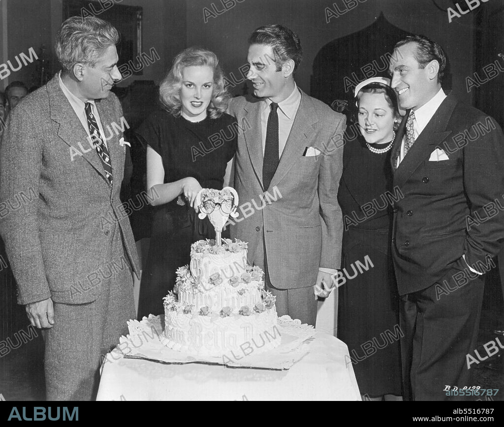 Harold Lloyd's Daughter In Screen Debut -- Blonde Gloria Lloyd, carrying on the film tradition of her talented parents, Harold and Mildred Lloyd, makes her screen debut in Universal-International's "Temptation," starring Merle Oberon, George Brent, Charles Korvin and Paul Lukas. Gloria is shown cutting her twenty-first birthday cake on the "Temptation" set. Notice her father's famed horn-rimmed spectacles adorning the top portion of the cake. Participants (left to right) include Director Irving Pichel, Gloria, Charles Korvin and Mildred and Harold Lloyd. Mrs. Lloyd, the former Mildred Davis, was leading lady in her husband's silent screen comedies. January 01, 1946. (Photo by Universal-International).