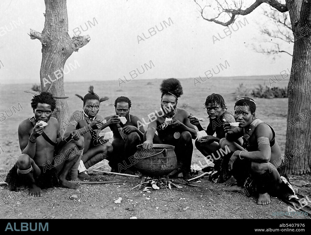 Six Zulu men posed sitting on the ground near a small cauldron, facing front, eating. The Zulus had a citizen army called up in times of war although all Zulu men were required to do military service when they reached the age of 19 until the age of 40 when they were allowed to marry. The Zulu Impi (army) were made up of regiments called Amabutho. Each regiment had its own identifying features either jewelry or a headdress. They were equipped with large cowhide shields which were color coded: younger regiments mostly black shields and older regiments more white. This allowed a Zulu general to identify the different units on the battlefield easily. Zulus carried a heavy broad bladed stabbing spear and a throwing spear. The warriors were highly disciplined and organized. They could travel fast and were highly mobile able to cover around 20 miles in a day and fight at the end of it or twice that distance in an emergency.  Frank and Frances Carpenter Collection, undated.