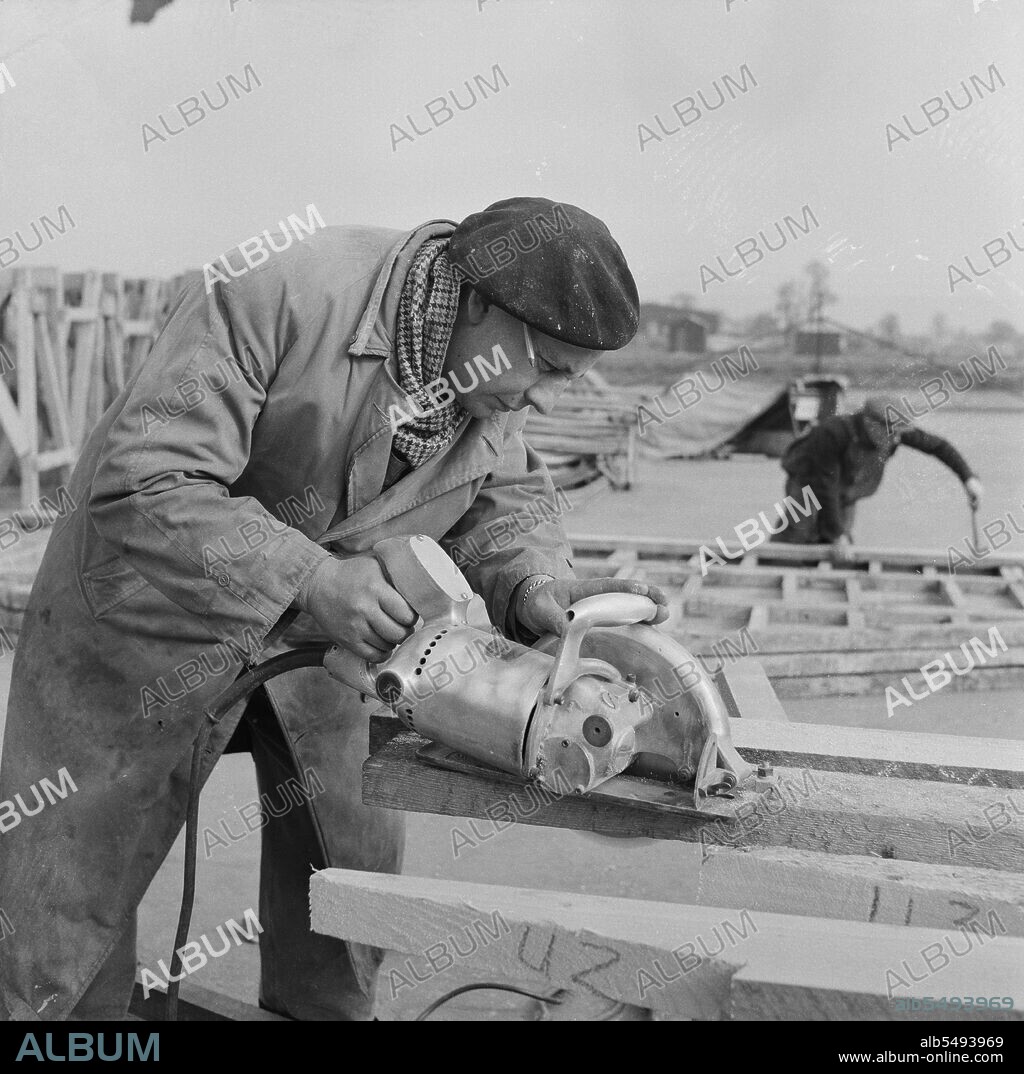 JOHN LAING PLC. RAF Gaydon, Gaydon, Stratford-on-Avon, Warwickshire, 11/03/1953. A workman using an electric circular saw to cut wood for use in the construction of buildings at Gaydon Airfield. Work began on the construction of a new runway at Gaydon Airfield in early 1952. This was followed by a second contract for the construction of more than 100 Easiform and Air Ministry buildings, and 23 Nissen huts.