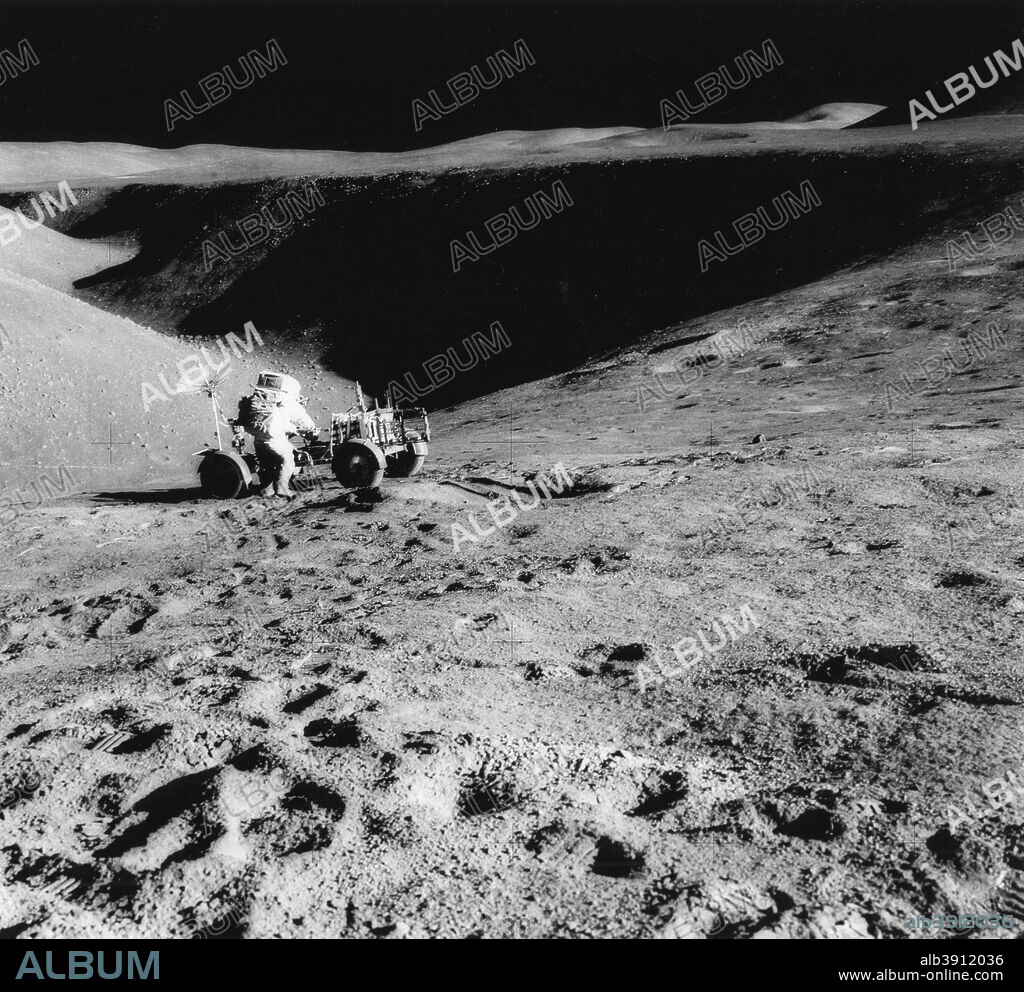 Astronaut David Scott (b1932) on the slope of Hadley Delta during Apollo 15, 1971. David Scott, mission commander, performs a task at the Lunar Roving Vehicle parked on the edge of Hadley Rille during the first Apollo 15 lunar surface extravehicular activity (EVA-1). This photograph was taken by Astronaut James B. Irwin, lunar module pilot, from the flank of St George Crater. The view is looking north along the rille.