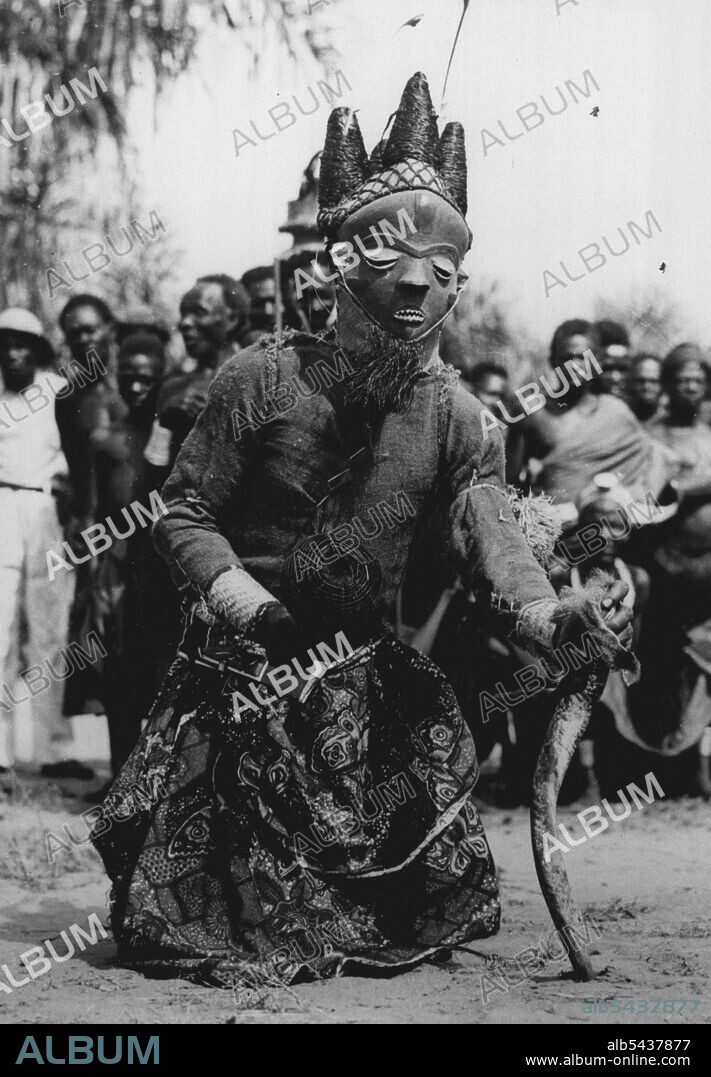 Congo Folklore -- Calling for the blessing of rain is this witch doctor during the Mbuya dance of the Bapende Tribe. In his right hand is basket filled with dried seeds, and in his left an antelope horn filled with mysterious powder. The Mbuya dance is an African Folklore 'Play' with as many as twenty characters. The Folklore of Africa lies, not in books, but in the Rhythmic Tribal dances that are handed down from generation to generation. The origins of the dances steps, the gestures and the s.
