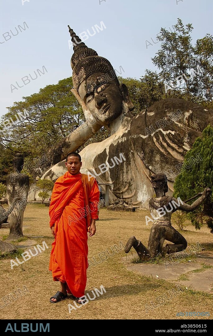 Buddhist monk wearing an orange robe in front of a Reclining Buddha statue, Buddha Park, Suan Xieng Khuan, near Vientiane, Laos, Southeast Asia, Asia.