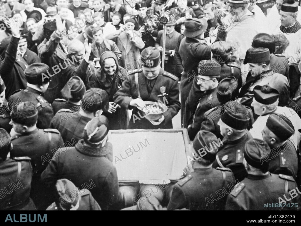 Mussolini says war will be fought to a finish - Mothers present trinkets to duce . Signor Mussolini with the helmet filled with trinkets which he had received from the old women at left . 20 December 1935.