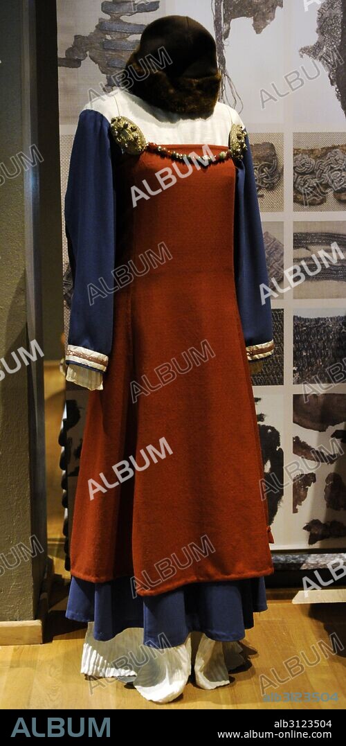 Traje femenino vikingo de clase acomodada. Vestido plisado con túnica azul y delantal rojo de lana. Zapatos típicos de época vikinga. Broches de bronce sostienen la ropa. Museo Histórico. Estocolmo. Suecia.